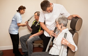 Carers helping two people with excersise machines